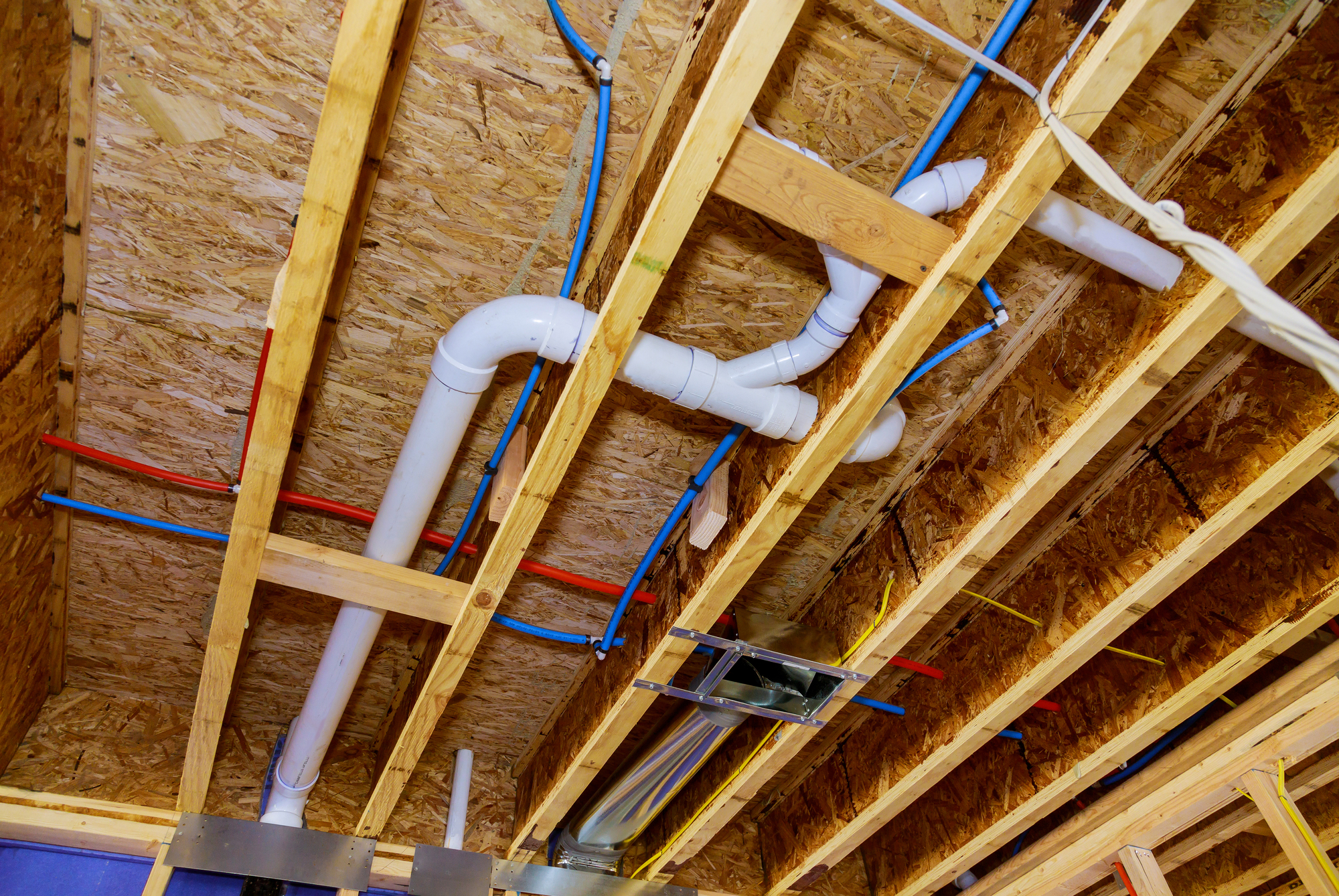 Exposed ceiling with wooden beams elegantly showcasing blue, red, and white pipes for plumbing, HVAC ductwork, and water lines.